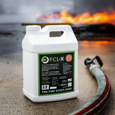 FCL-X concentrate jug next to a fire hose, with a fire burning behind